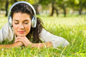 Closeup portrait of beautiful young woman laying on grass and listening to music with headphones